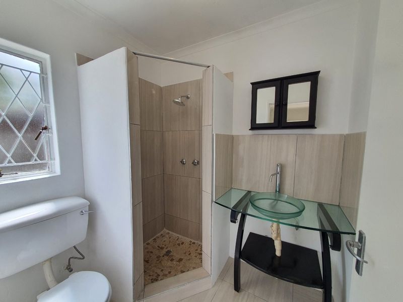 A functional bathroom featuring a tiled shower enclosure, a glass vessel sink with a vanity console, and a wall-mounted medicine cabinet.