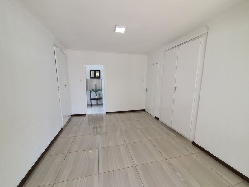 A clean, empty bedroom featuring neutral tiled flooring, built-in cupboards, and direct access to an en-suite bathroom area.