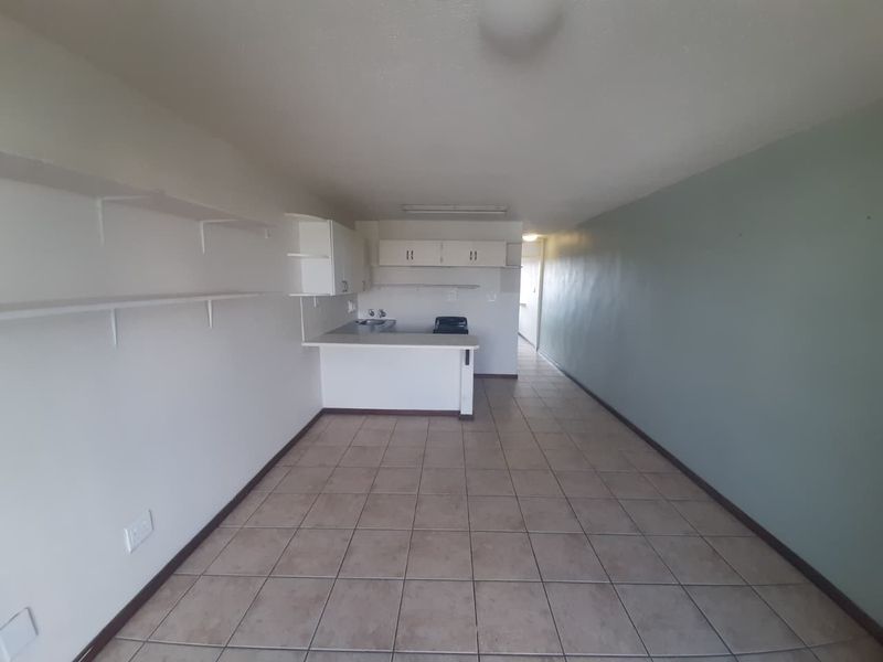 An empty open-plan living and kitchen area featuring tiled flooring, built-in cabinetry, a breakfast counter, and wall-mounted shelving.