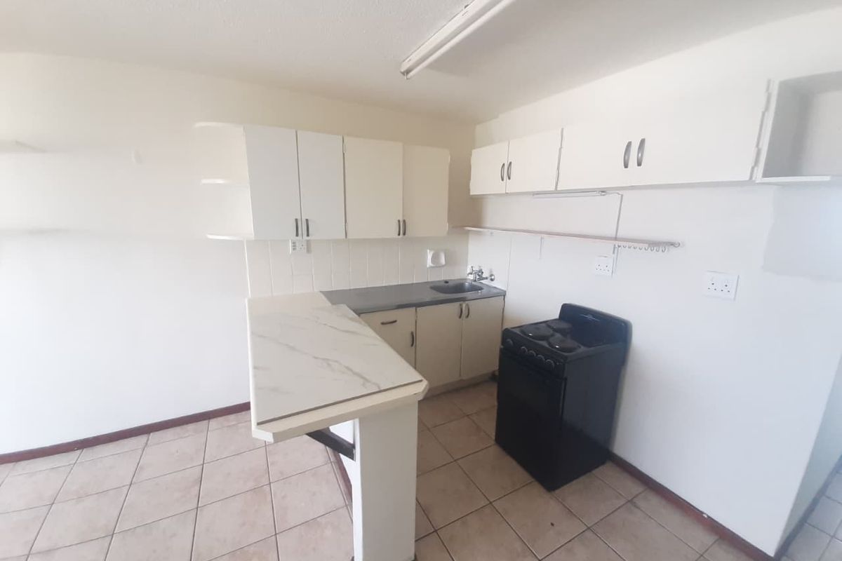 A compact kitchen featuring built-in cabinetry, a breakfast bar, tiled flooring, and a freestanding stove, offering a functional space ready for modernization.