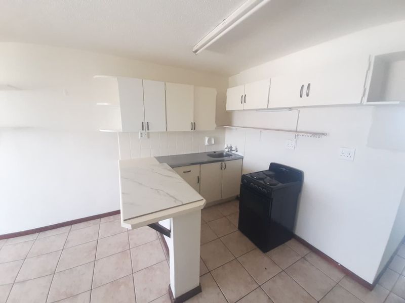 A compact kitchen featuring built-in cabinetry, a breakfast bar, tiled flooring, and a freestanding stove, offering a functional space ready for modernization.