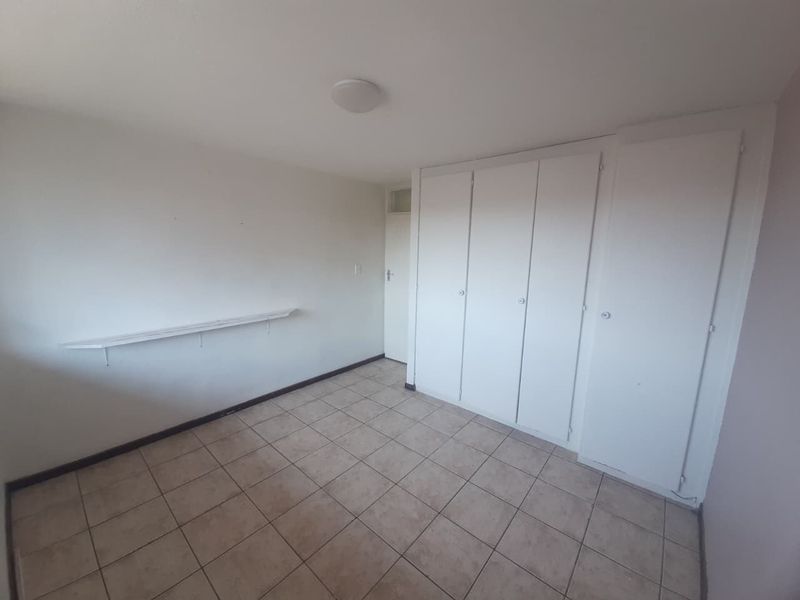 A clean, empty bedroom featuring neutral tiled flooring and ample built-in cupboard storage space.