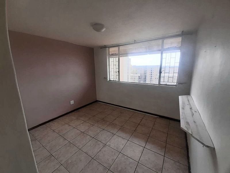 An empty bedroom featuring tiled flooring, a wall-mounted shelf, and large windows with security bars, offering a blank canvas for potential renovation.