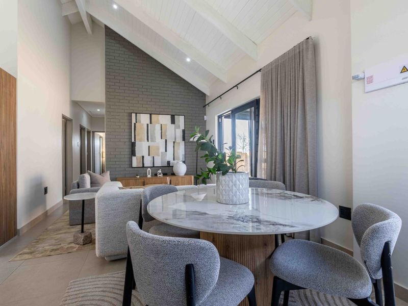 Modern open-plan living and dining area featuring a high vaulted ceiling, exposed brick feature wall, and large sliding glass doors for natural light.