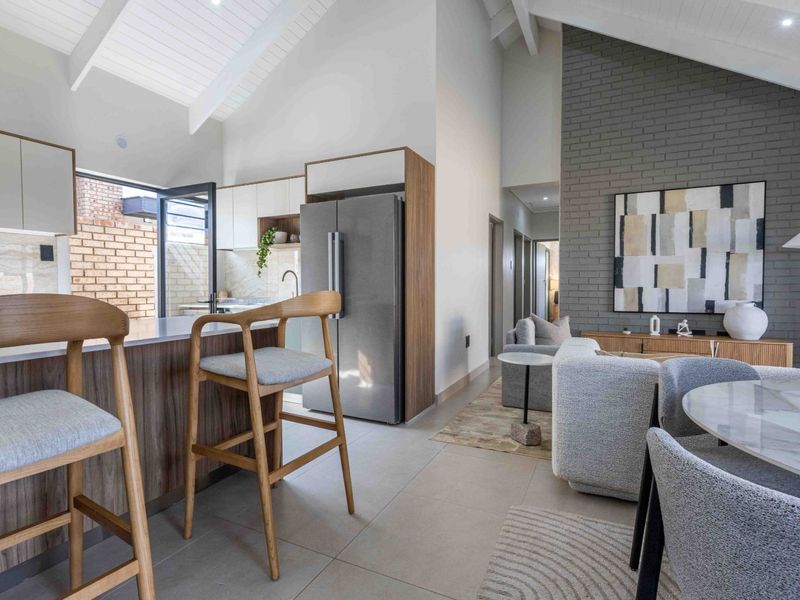 Modern open-plan living area featuring a vaulted ceiling, exposed brick feature wall, and a contemporary kitchen with a central island and high-quality finishes.