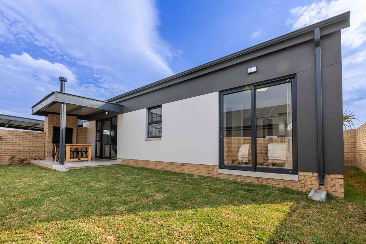 Rear view of the property featuring a covered patio with a built-in braai, sliding glass doors, and a well-maintained garden.