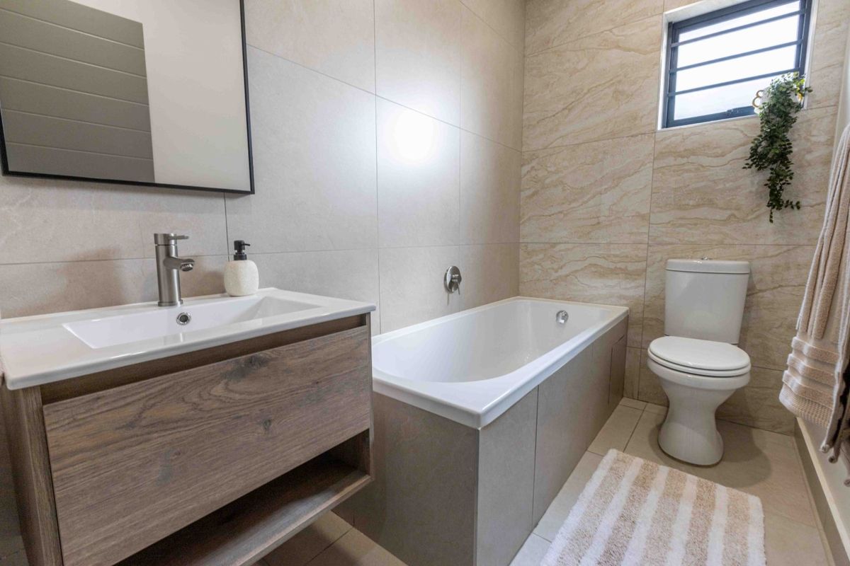 Modern bathroom featuring a vanity cabinet with basin, bathtub, and toilet, finished with neutral wall and floor tiling.