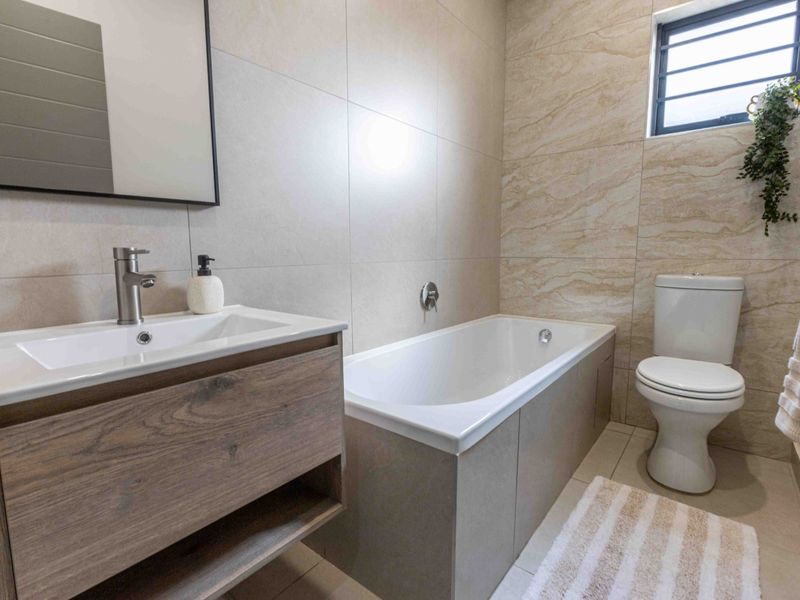 Modern bathroom featuring a vanity cabinet with basin, bathtub, and toilet, finished with neutral wall and floor tiling.