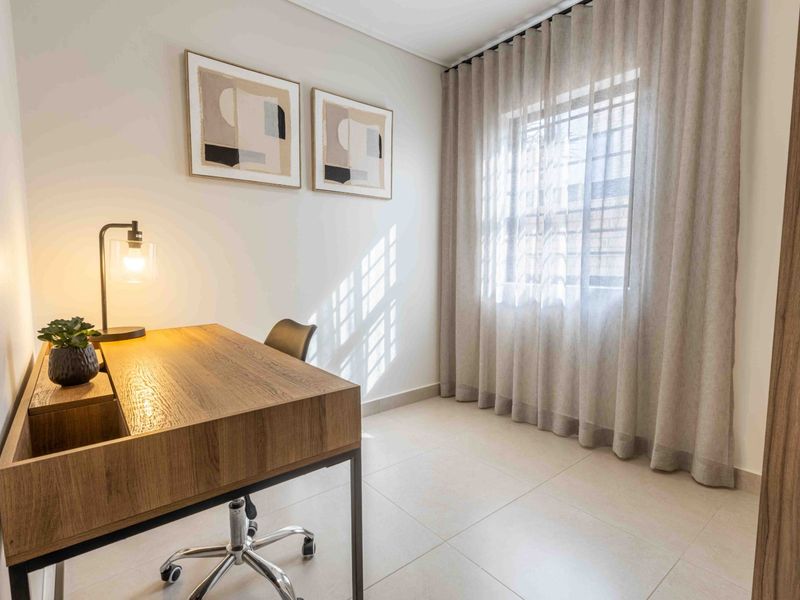 A bright and modern home office featuring neutral tiled flooring, large windows with elegant curtains, and integrated security bars.
