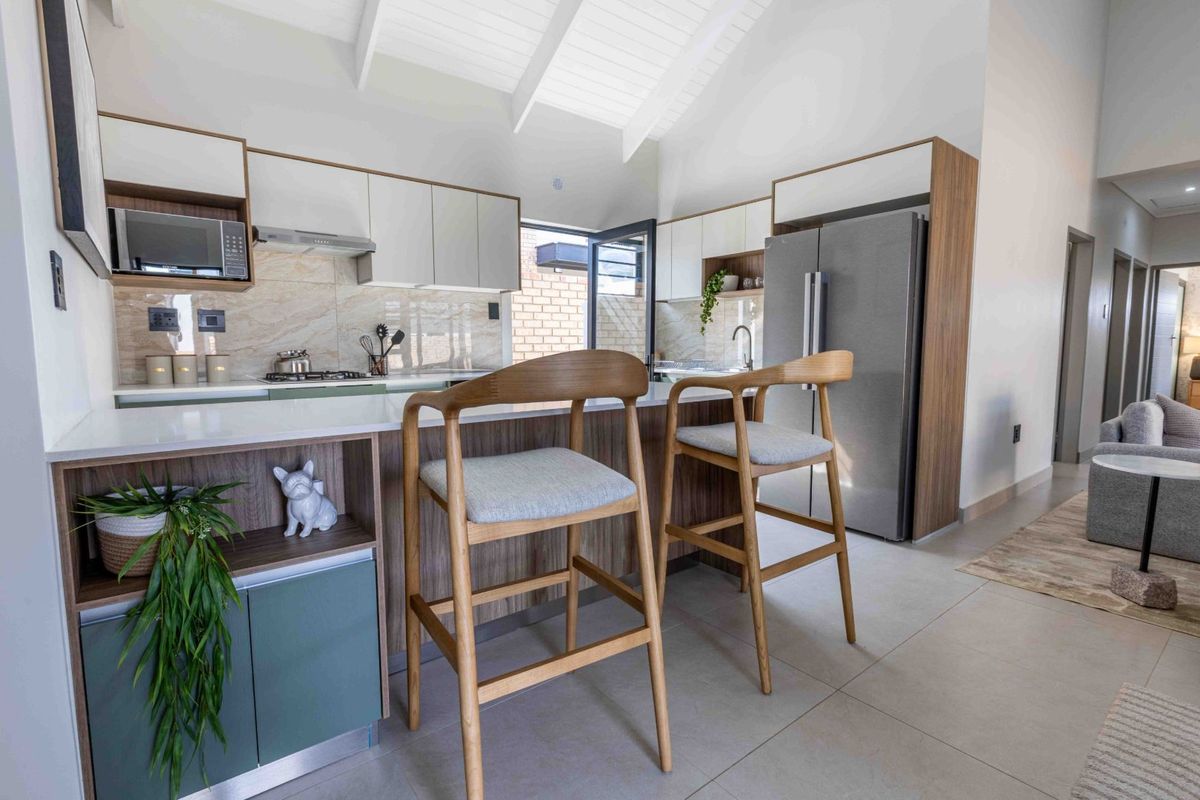 Modern kitchen featuring sleek built-in cabinetry, stone countertops, integrated appliances, and a vaulted ceiling, seamlessly flowing into the adjacent living area.