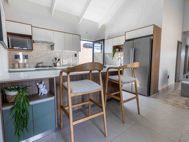 Modern kitchen featuring sleek built-in cabinetry, stone countertops, integrated appliances, and a vaulted ceiling, seamlessly flowing into the adjacent living area.