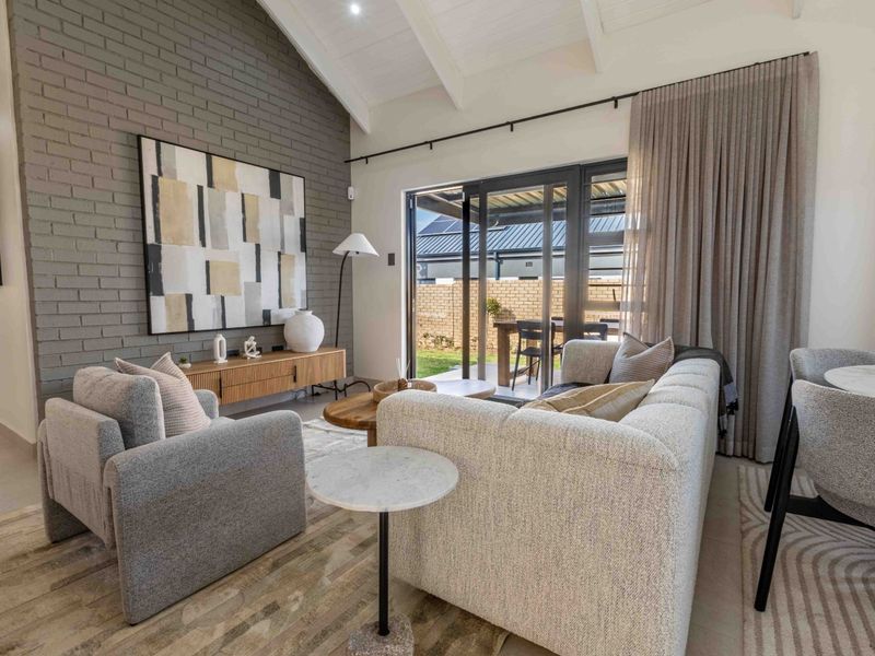 Bright open-plan living area featuring a vaulted ceiling, exposed brick feature wall, and large sliding glass doors leading to an outdoor patio.