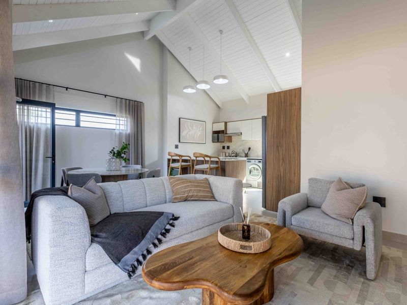 Modern open-plan living area featuring a vaulted ceiling with exposed beams, integrated kitchen cabinetry, and high-quality finishes throughout.