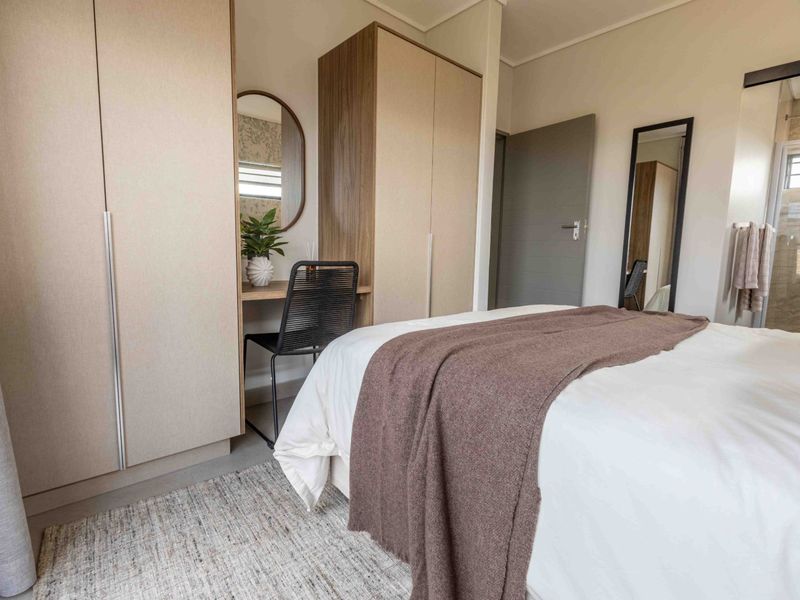 A well-maintained bedroom featuring neutral-toned built-in cupboards with an integrated vanity area and modern tiled flooring.