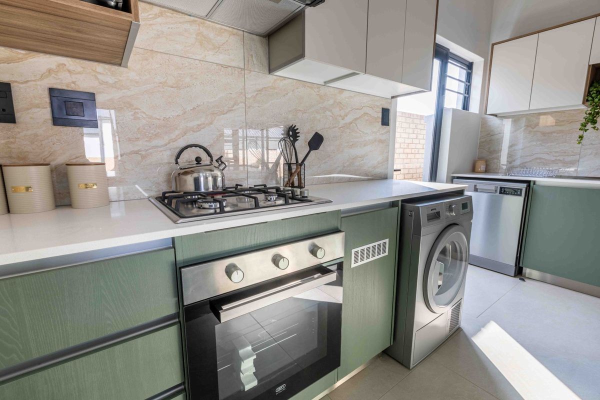 Modern kitchen featuring green cabinetry, stone countertops, built-in oven, gas hob, extractor fan, and integrated laundry and dishwasher appliances.