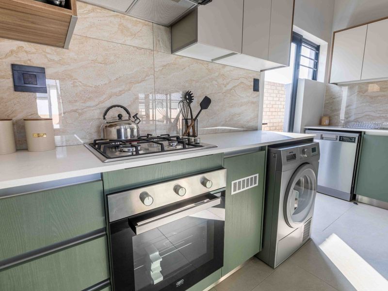 Modern kitchen featuring green cabinetry, stone countertops, built-in oven, gas hob, extractor fan, and integrated laundry and dishwasher appliances.