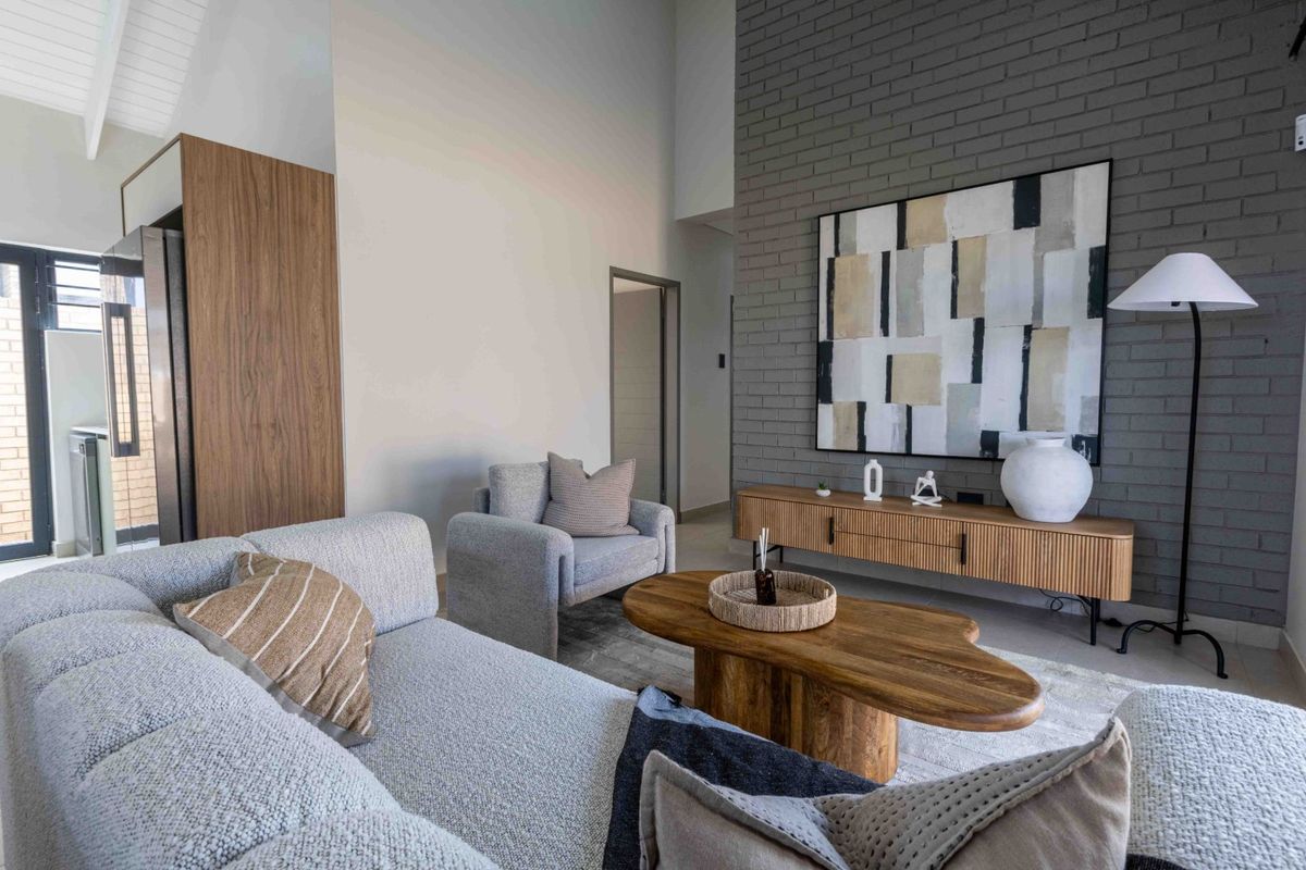 A modern living room featuring a striking grey exposed brick feature wall, high vaulted ceilings, and natural light from a large sliding glass door.