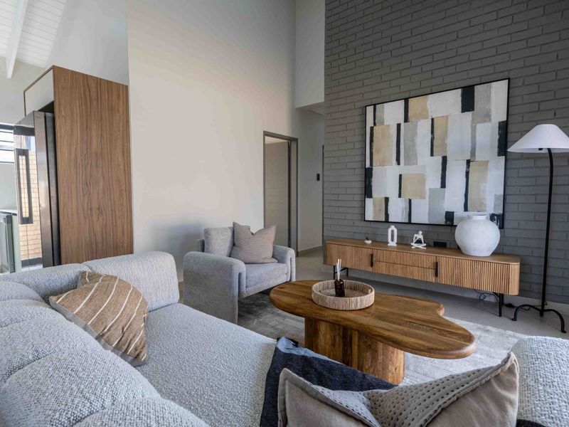 A modern living room featuring a striking grey exposed brick feature wall, high vaulted ceilings, and natural light from a large sliding glass door.