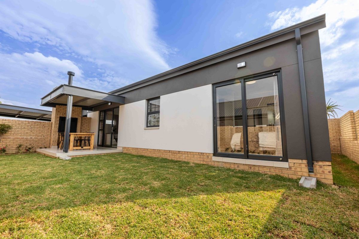 Rear view of the property featuring a covered patio with a built-in braai, sliding glass doors, and a well-maintained garden area.