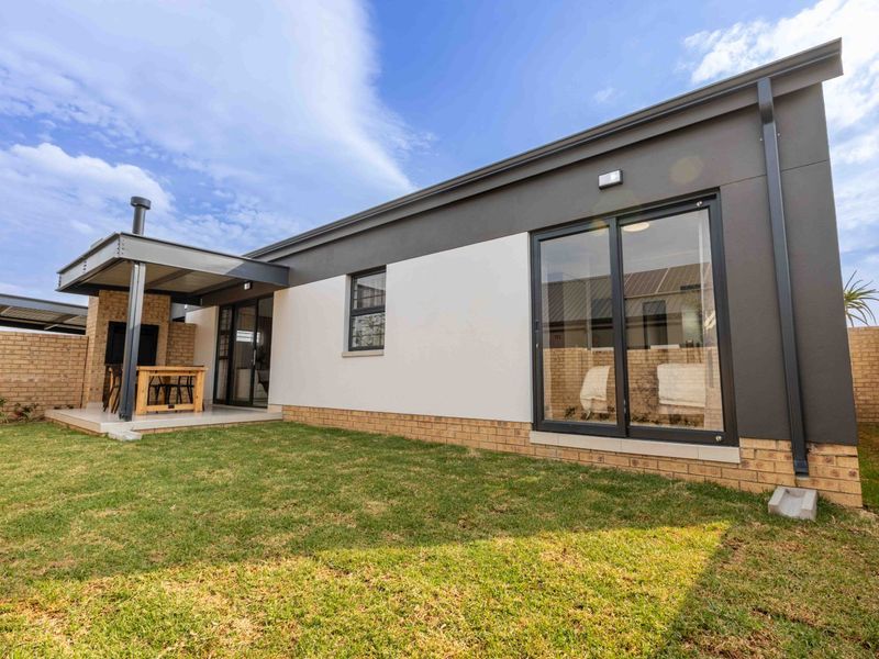 Rear view of the property featuring a covered patio with a built-in braai, sliding glass doors, and a well-maintained garden area.