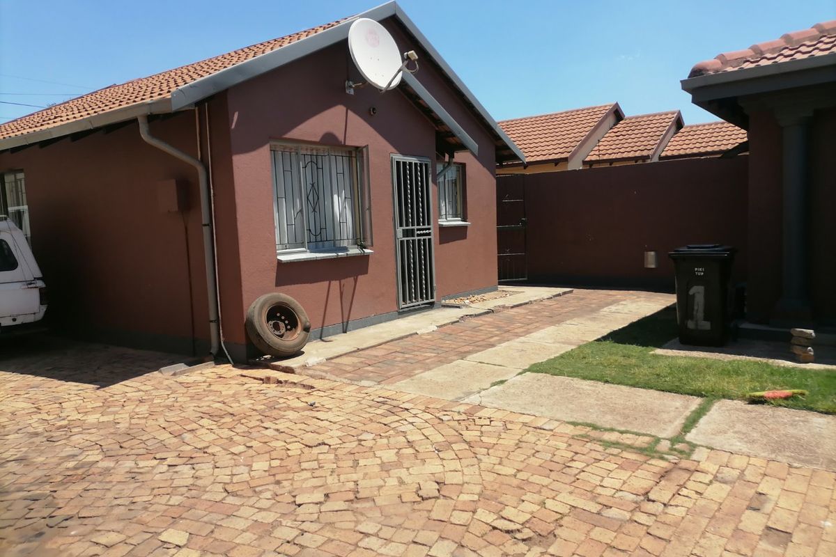 Rear exterior view of the property featuring a tiled roof, security gates, and paved driveway area.