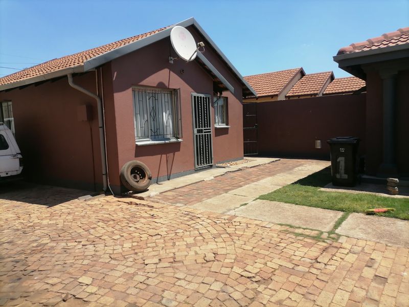 Rear exterior view of the property featuring a tiled roof, security gates, and paved driveway area.