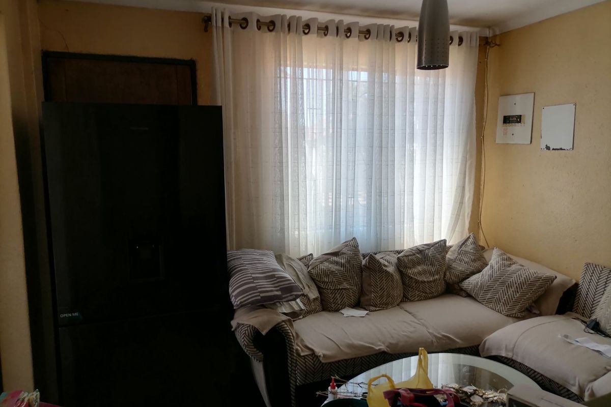 A living room area featuring a window with curtain rails and a pendant light fixture, showing signs of wear on the wall surfaces.