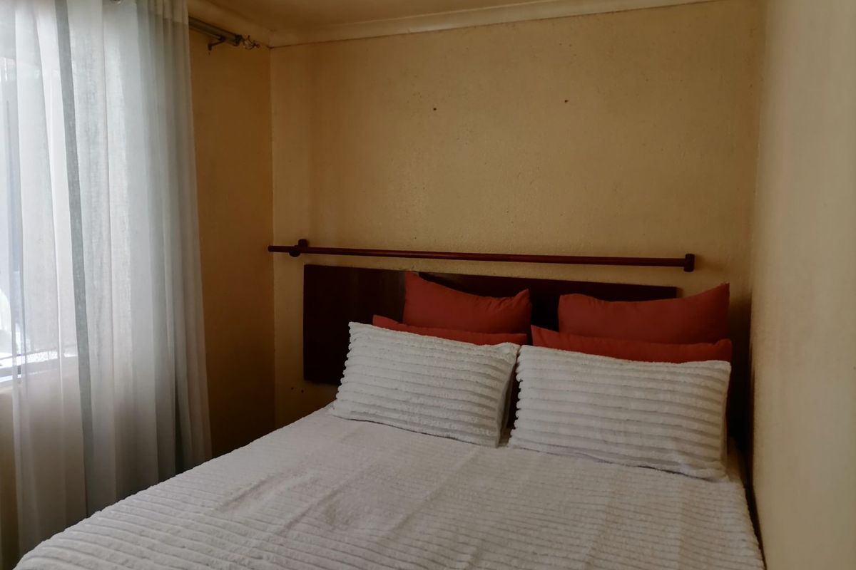 A compact bedroom featuring a window with a curtain rail and plain wall finishes, requiring cosmetic updates to improve the overall aesthetic.