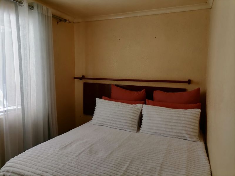 A compact bedroom featuring a window with a curtain rail and plain wall finishes, requiring cosmetic updates to improve the overall aesthetic.