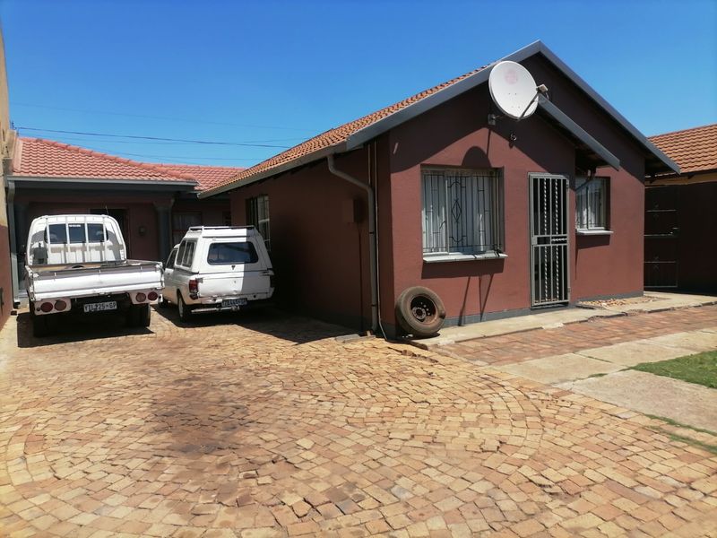 Front exterior view of the house featuring a paved driveway, tiled roof, and security features including burglar bars and security gates.