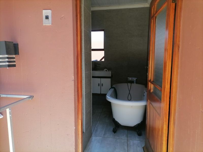 A bathroom featuring a classic freestanding bathtub, vanity cabinet with basin, and neutral wall and floor tiling, viewed from an adjacent exterior space.
