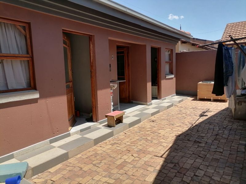 Rear exterior view of the property featuring a paved courtyard, multiple access points, and a boundary wall.