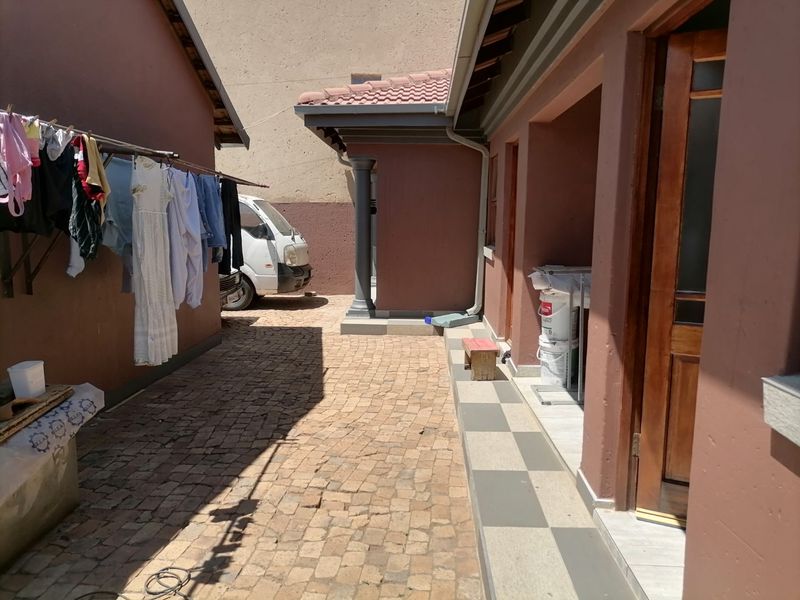 A paved rear exterior area featuring a tiled patio section, guttering, and access to the main building via a wooden door.