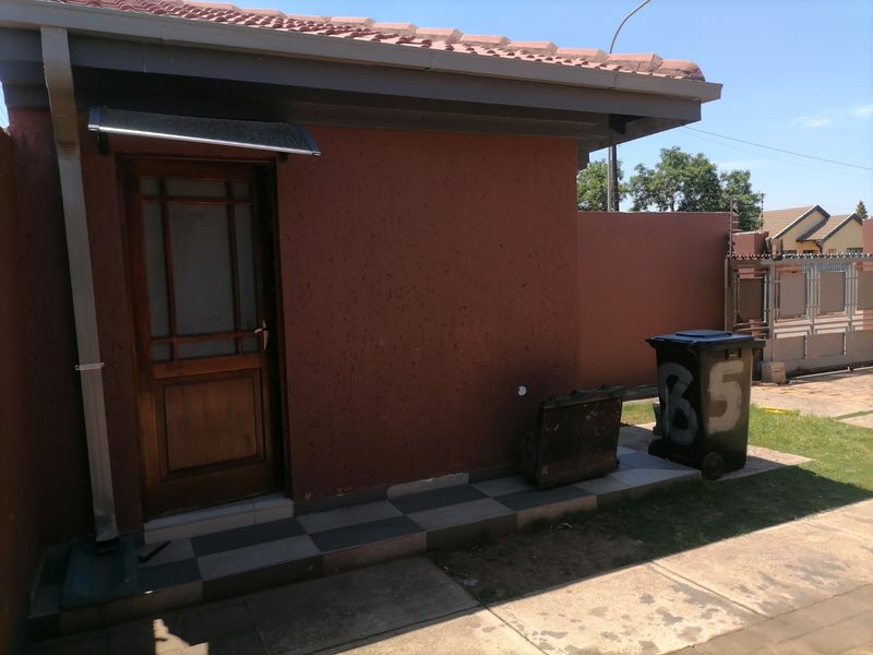 Rear exterior view of the property featuring a timber door, protective canopy, and paved walkway along the perimeter wall.