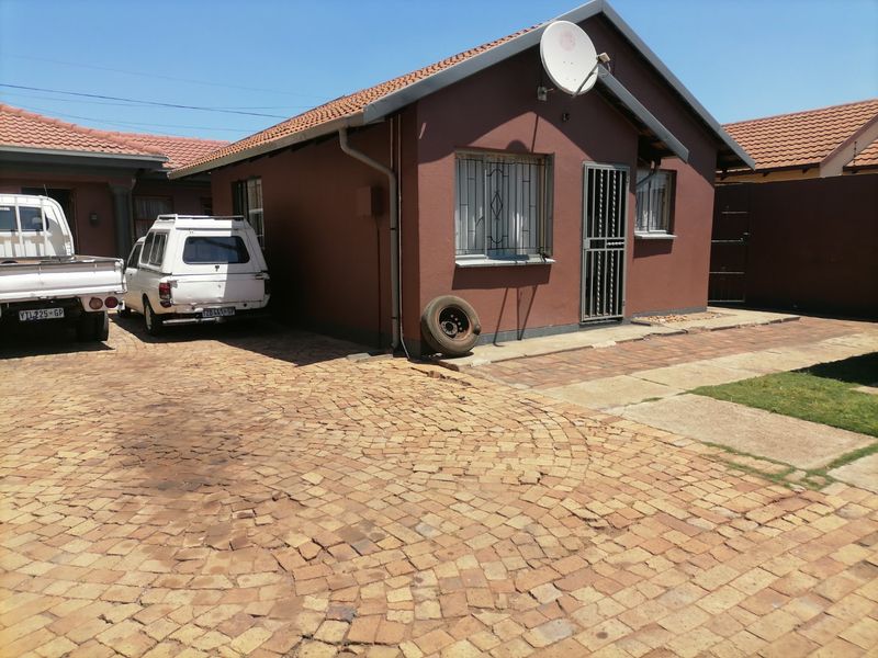 Front exterior view of a residential house featuring a tiled roof, brick paved driveway, and security fixtures including burglar bars and a security gate.
