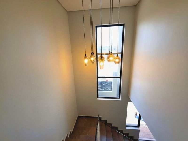 A bright and modern double-volume stairwell featuring elegant pendant lighting, large windows, and clean tiled flooring.