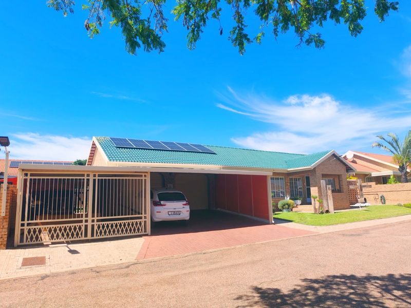 Front view of a brick house featuring a green tiled roof with solar panels, a paved driveway, and a covered carport area.