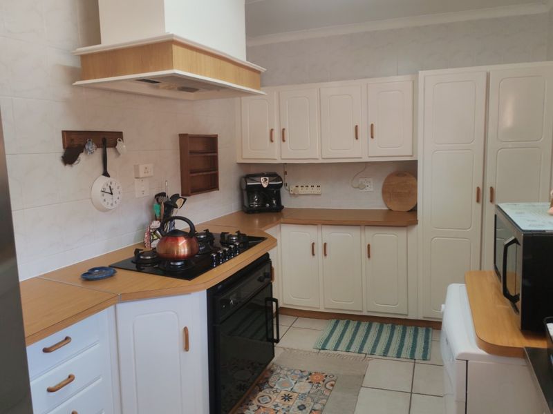 A functional kitchen featuring white cabinetry, laminate countertops, a gas hob, built-in oven, and tiled splashbacks with neutral floor tiles.