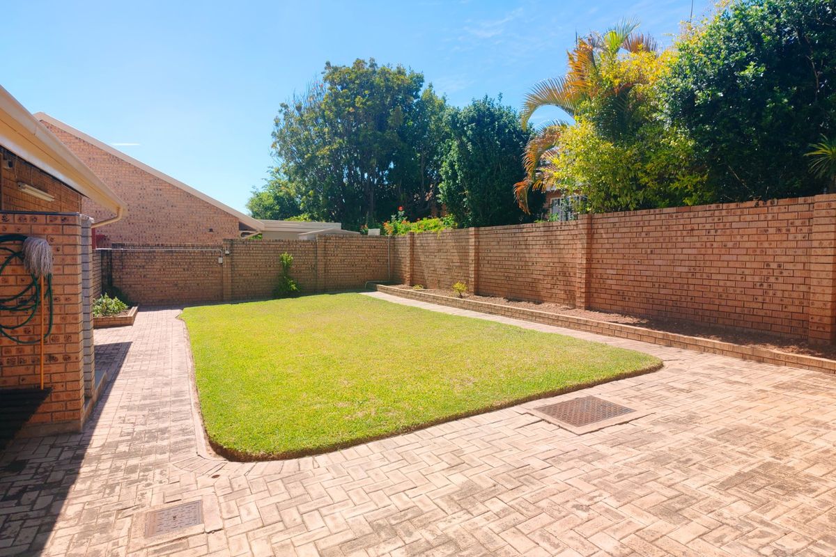 A well-maintained rear garden featuring a central lawn area, paved surround, and solid brick boundary walls.