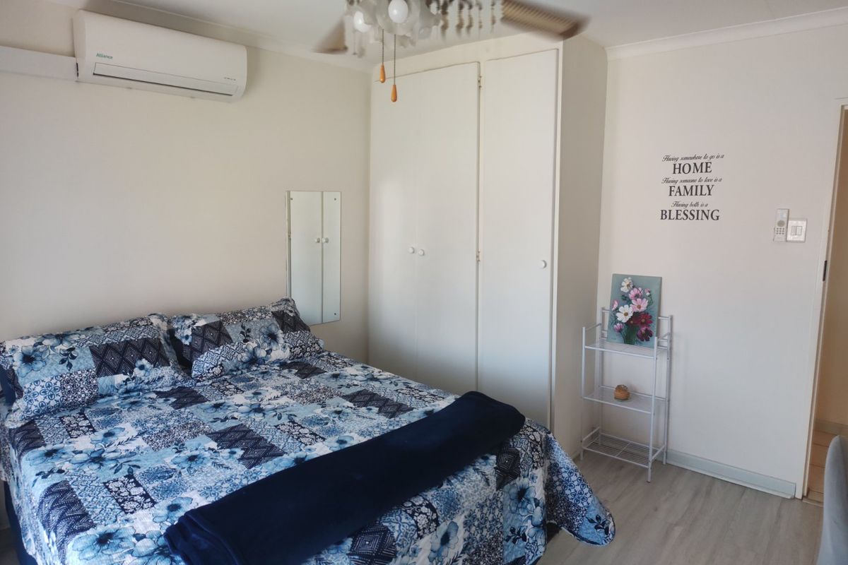 A well-maintained bedroom featuring built-in cupboards, a ceiling fan, and an air conditioning unit, finished with modern laminate flooring.