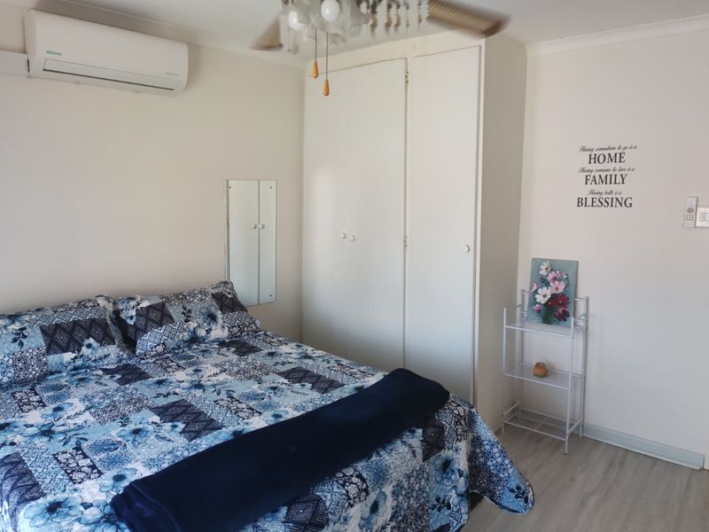 A well-maintained bedroom featuring built-in cupboards, a ceiling fan, and an air conditioning unit, finished with modern laminate flooring.