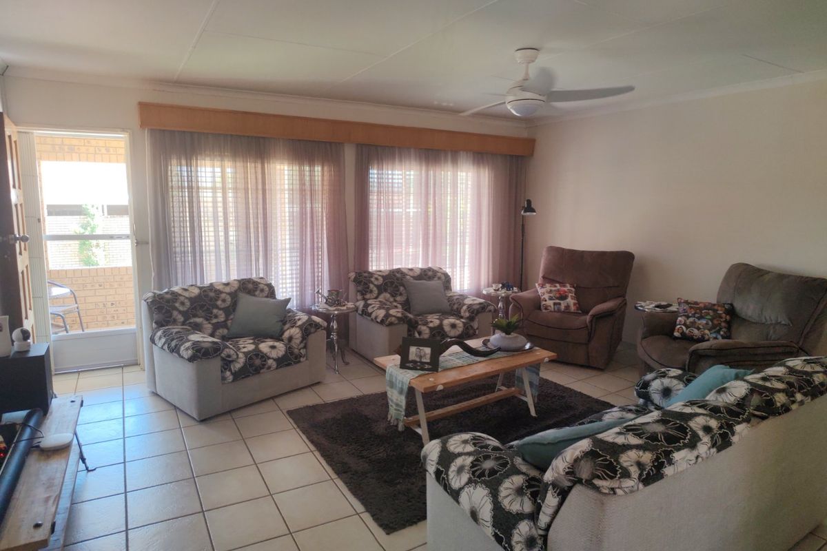 A comfortable living room featuring tiled flooring, a ceiling fan, and large windows with curtains, providing direct access to an outdoor patio area.