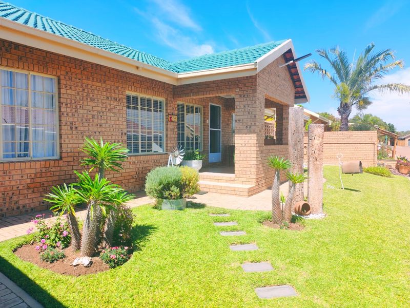 A well-maintained face brick house featuring a covered entrance porch, tiled roof, and a neat landscaped garden with a paved walkway.