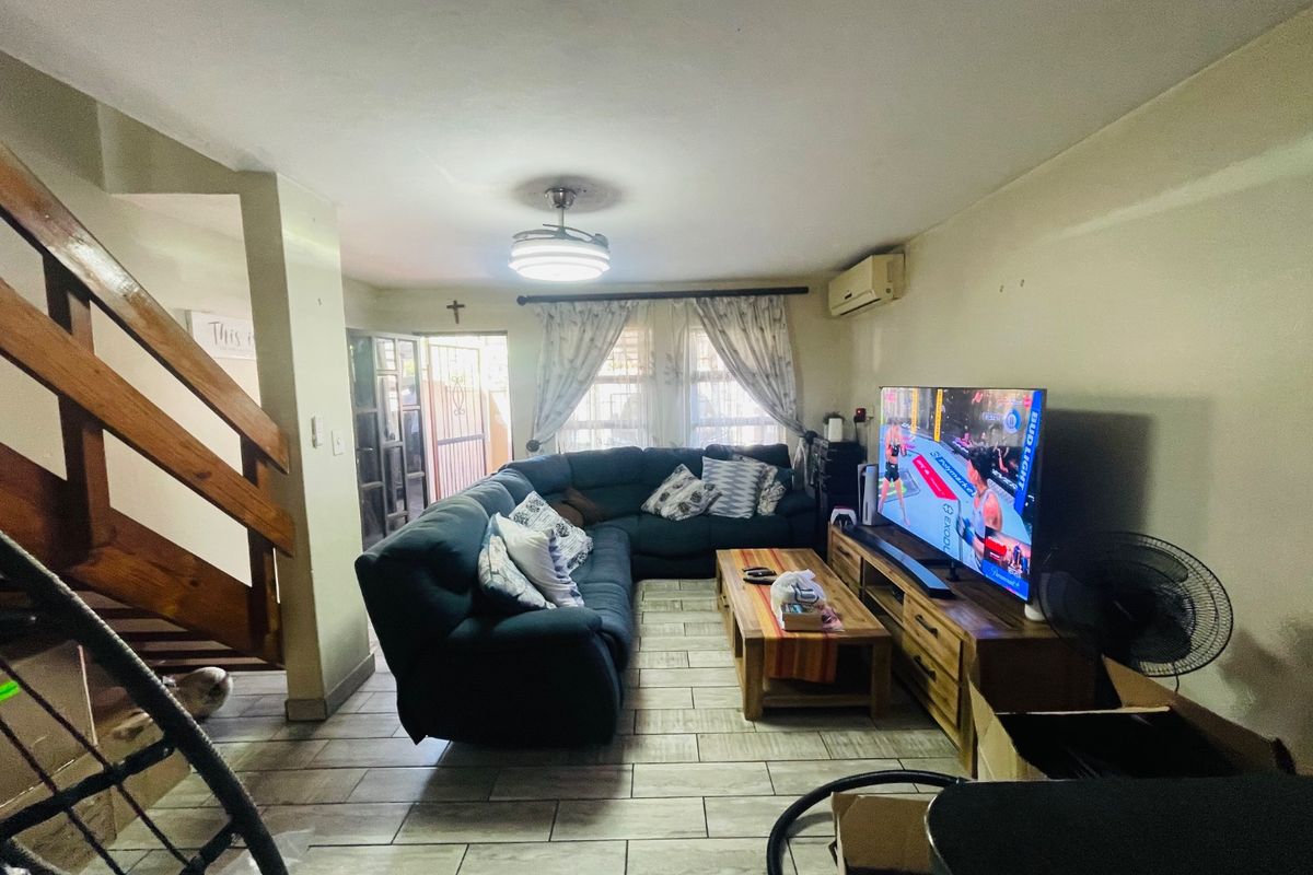 A functional living room featuring tiled flooring, a ceiling fan, and a split-system air conditioner, with a wooden staircase leading to the upper level.
