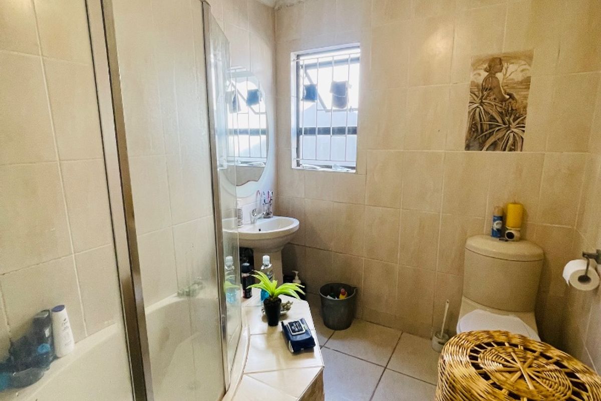 A functional bathroom featuring a shower enclosure, pedestal basin, and toilet, finished with neutral wall and floor tiling.