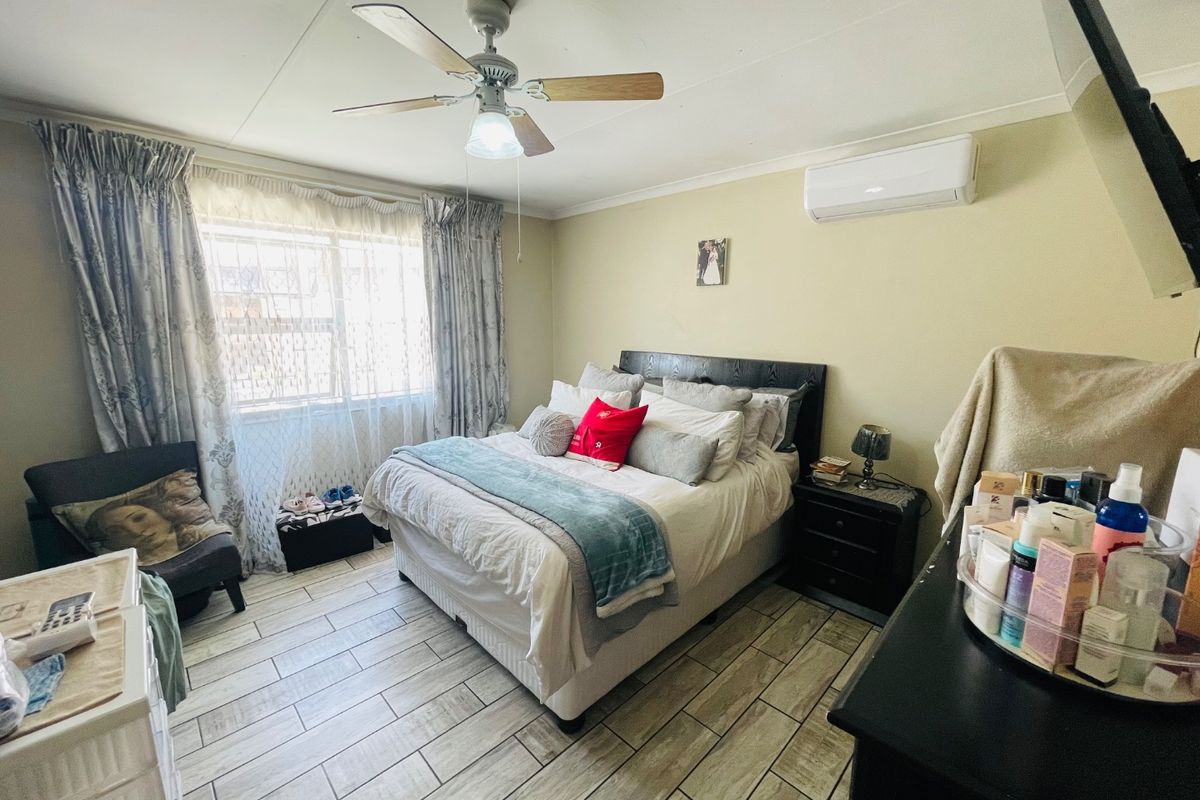 A functional bedroom featuring tiled flooring, a ceiling fan, and a wall-mounted split-system air conditioner.