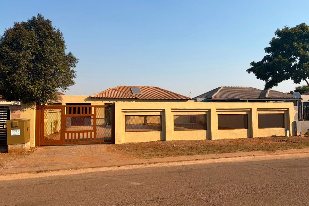 Front exterior view of the townhouse featuring a secure perimeter wall, metal driveway gate, paved driveway, and a tiled roof with a solar panel.