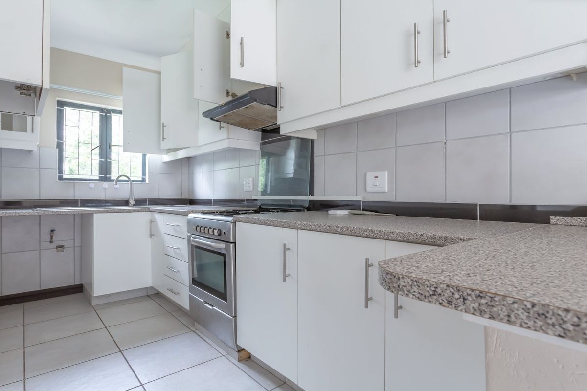 A functional kitchen featuring white cabinetry, granite-look countertops, a stainless steel oven and hob, and tiled finishes throughout.