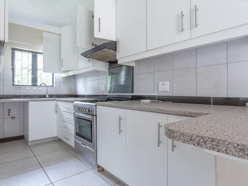 A functional kitchen featuring white cabinetry, granite-look countertops, a stainless steel oven and hob, and tiled finishes throughout.