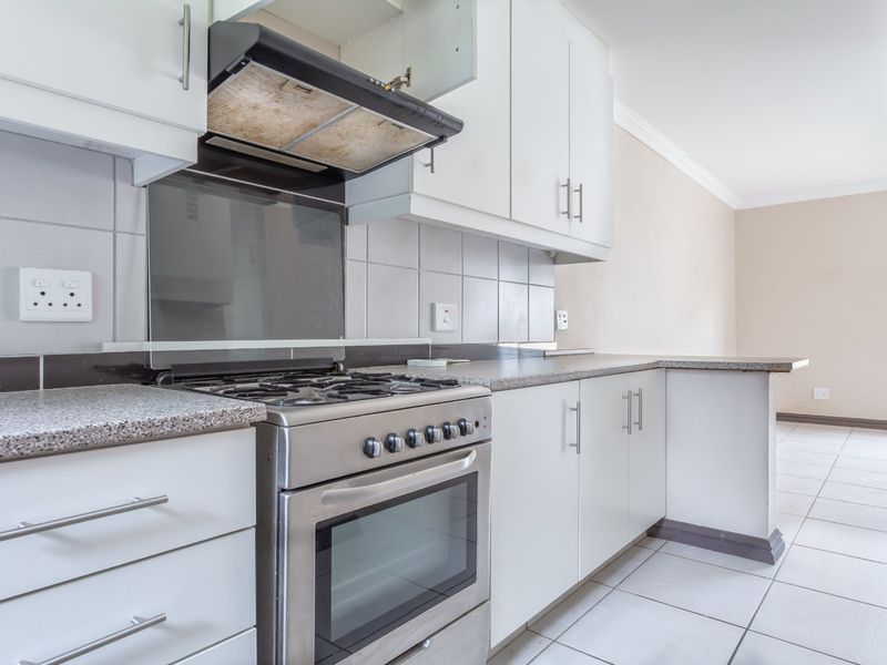 A functional kitchen featuring white cabinetry, granite countertops, a stainless steel gas stove, and tiled flooring, offering a clean and practical workspace.